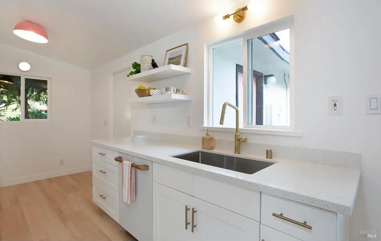 Kitchen sink with brass fixtures, quartz counters, and open shelving